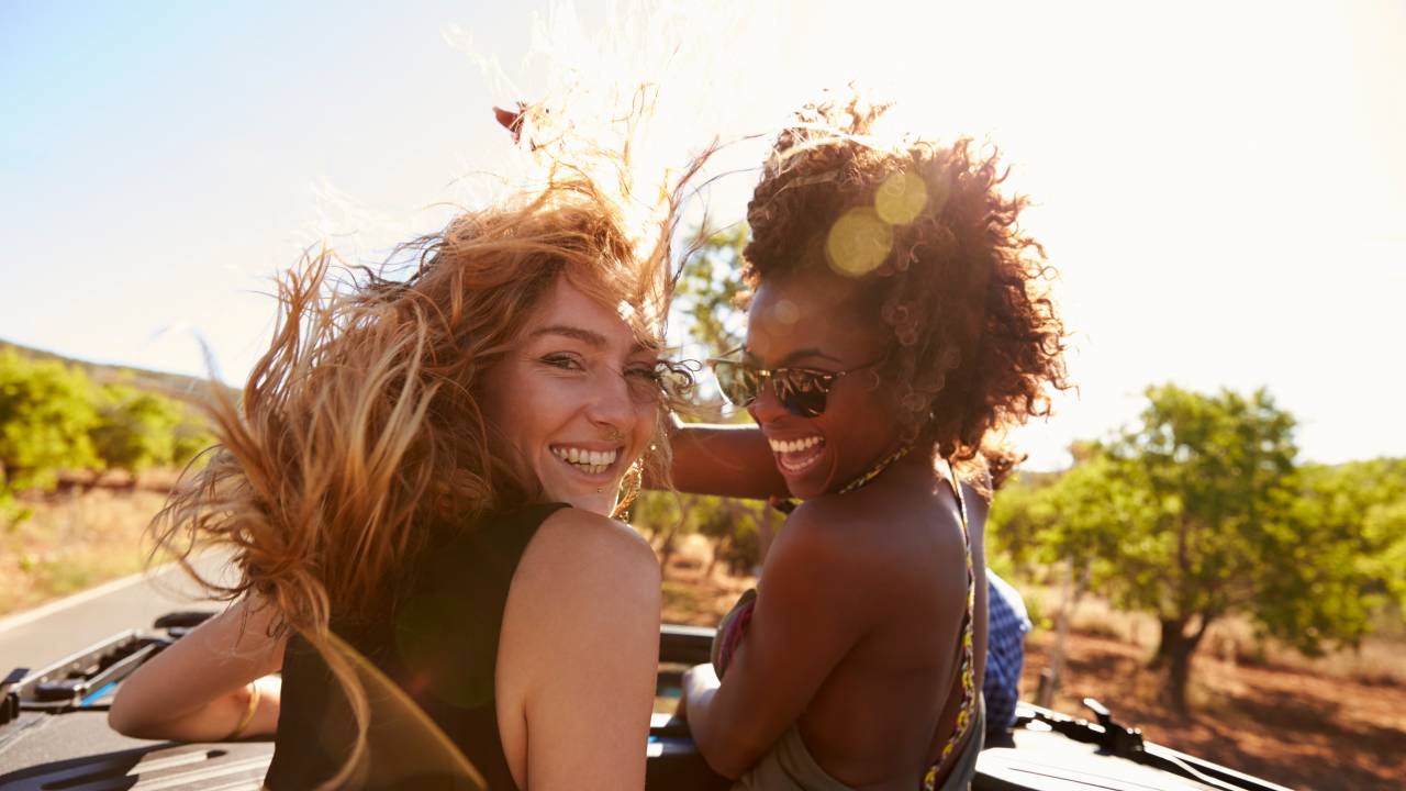 Duas mulheres viajantes percorrem estrada com carro conversível olhando para trás