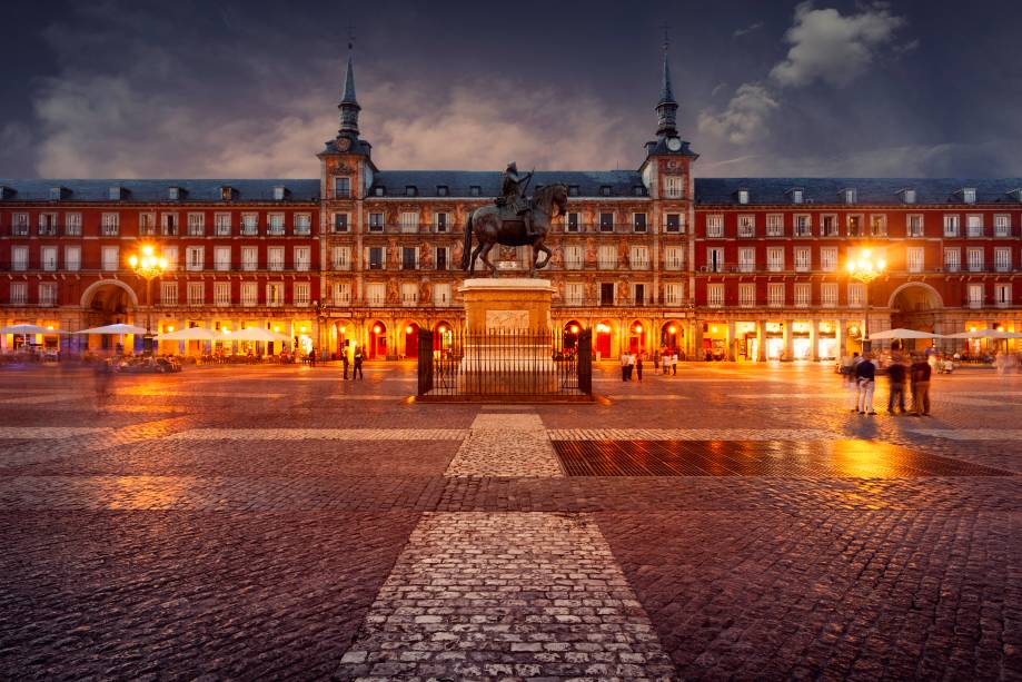 <strong>Plaza Mayor – <a href="https://gutenberg.viagemeturismo.abril.com.br/cidades/madri/" target="_blank" rel="noopener">Madri</a> – <a href="https://gutenberg.viagemeturismo.abril.com.br/paises/espanha/" target="_blank" rel="noopener">Espanha</a></strong> Boa parte das cidades espanholas e mesmo aquelas fundadas e conquistadas por eles nas Américas têm sua <strong>Plaza Mayor</strong>. Centro gravitacional da vida cívica, mercado e sede de edifícios governamentais, tudo girava ao seu redor. A mais bela e definitiva dessas praças não poderia estar em outro lugar, senão na capital do país. Ao longo de sua história, a Plaza Mayor de Madri foi palco de touradas, execuções e autos de fé da radical Inquisição espanhola, um local onde igreja e coroa atestavam seu poder perante o povo. O formato retangular e a relativa simetria no desenho dos edifícios é obra de sucessivos monarcas, mas boa parte das atuais características se devem a Filipe III, cuja estátua está fixada no centro da praça. Cafés e restaurantes espalham sob as arcadas centenas de mesas durante o dia, um ótimo lugar para ver a vida passar  <em>Busque hospedagem em Madri</em>