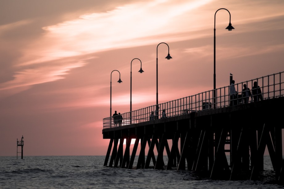 Pessoas observam o pôr do sol no cais de Glenelg, na cidade australiana de Adelaide