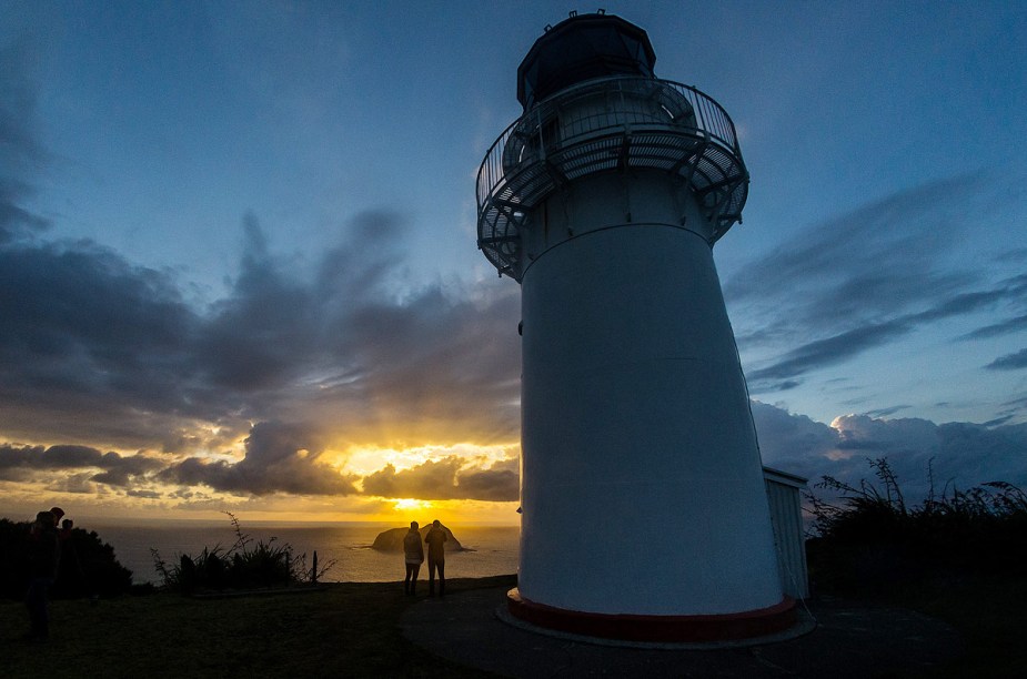 Turistas observam o pôr do sol a partir do farol de Gisborne