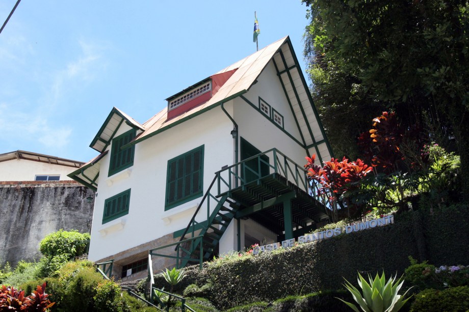 A <a href="https://viajeaqui.abril.com.br/estabelecimentos/br-rj-petropolis-atracao-casa-de-santos-dumont" rel="Casa de Santos Dumont" target="_blank">Casa de Santos Dumont</a> (A Encantada) é outra construção que vale a visita em Petrópolis (RJ). Considerada moderna na época (foi erguida em 1918), a pequena construção alpina de três pavimentos apresenta todas as criações de Santos Dumont, exceto evidentemente o 14-Bis. Lá estão o chuveiro quente movido a álcool, a famosa escada para apenas um pé (comece subindo com o esquerdo) e os móveis colados na parede. Só não espere encontrar uma cozinha: parece que Dumont não era bom nessa área e um hotel vizinho preparava suas refeições.<br />       