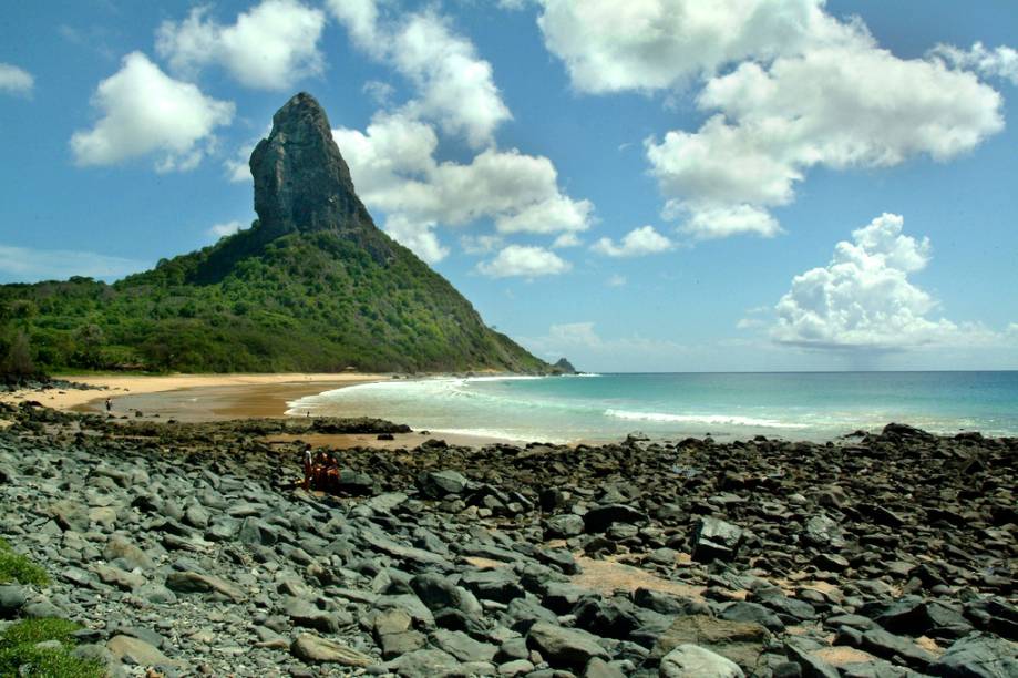 <a href="https://viajeaqui.abril.com.br/estabelecimentos/br-pe-fernando-de-noronha-atracao-praia-da-conceicao"><strong>Praia da Conceição</strong></a>Esta praia tem algo raro em Noronha: um bar pé na areia, o Duda Rei. Tome uma cervejinha e belisque um queijo coalho grelhado enquanto avista o Morro do Pico, faça uma caminhada pela extensa faixa de areia e, se a maré estiver baixa, explore as piscinas naturais que se formam no lado direito da praia. De  abril a novembro, o mar fica calmo, mas de dezembro a março a praia é dos surfistas, com ondas de 1,5 metro. Sorte de quem estiver hospedado na Vila do Trinta ou na Vila dos Remédios, que consegue vir até a Praia da Conceição a pé.