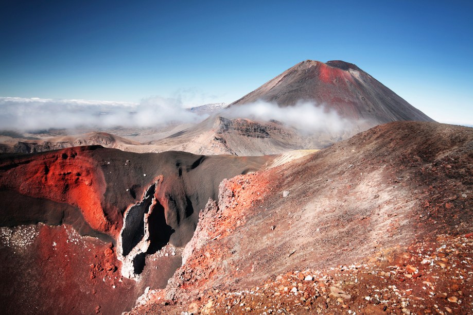 <a href="http:// https://viajeaqui.abril.com.br/paises/nova-zelandia" target="_blank" rel="noopener"><strong>Tongariro, Nova Zelândia</strong></a> Este belo vulcão é um dos três ativos da ilha norte da Nova Zelândia. Com 1.978m de altitude em seu cume mais alto, é composto por um maciço com pelo menos 12 cones. O nome deriva das palavras maori “tonga” (vento sul) e “riro” (arribado, aportado), que veio de uma lenda. Senta que lá vem história: <em>Segundo a lenda, o grande navegador Ngatoroirangi, padre da migração Arawa no século XIV, escalou o Tongariro e, chegando lá em cima, enquanto ele perecia no cume da grande montanha e esperando que os deuses lhe enviassem fogo, ele disse “Ka riro au I te tonga” (Eu estou aportado no amargo vento sul)</em>.