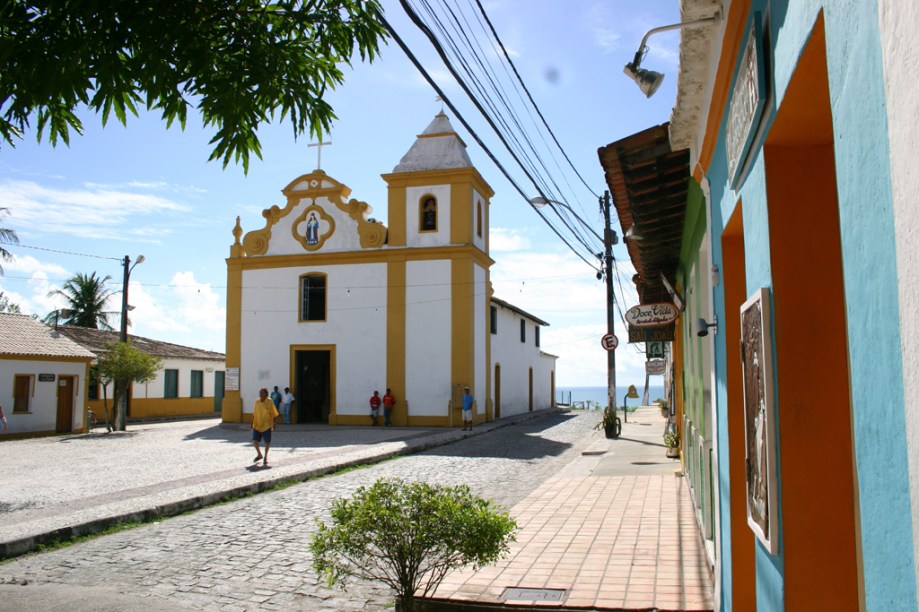 A Igreja de Nossa Senhora d’Ajuda foi erguida no centro de Arraial dAjuda em 1549. O mirante atrás da Igreja oferece uma visão panorâmica que tem o Arraial d’Ajuda Eco Park em primeiro plano e, ao fundo, o mar azul de Porto Seguro na Bahia