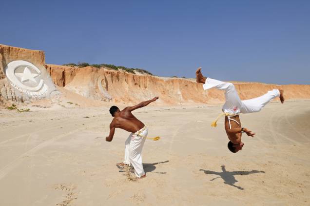 Capoeiristas na praia do centrinho de Canoa Quebrada. Ao fundo, o símbolo do destino esculpido na pedra Capoeiristas na praia do centrinho de Canoa Quebrada. Ao fundo, o símbolo do destino esculpido na pedra
