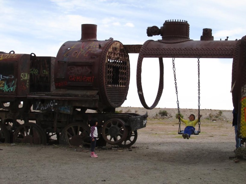 Crianças brincando no cemitério de trens em Uyuni, Bolívia