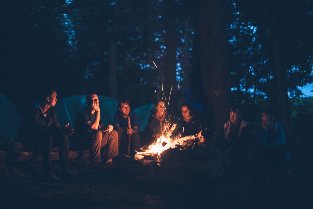 Turma de amigos acampando e sentados em volta da fogueira, à noite