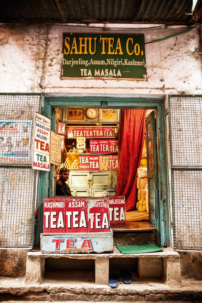 Uma loja simplória de chá, de portas abertas, com grandes caixas de diferentes sabores de chá, todas elas com a palavra 