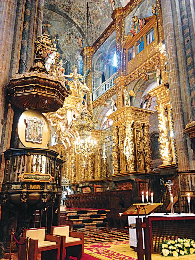 Interior de uma catedral, com tetos altos, pisos de ladrilho de diferentes padrões e grupos de pequenas colunas suportando a estrutura, assim como pinturas e estátuas de santos e madonas, grande parte em ouro.