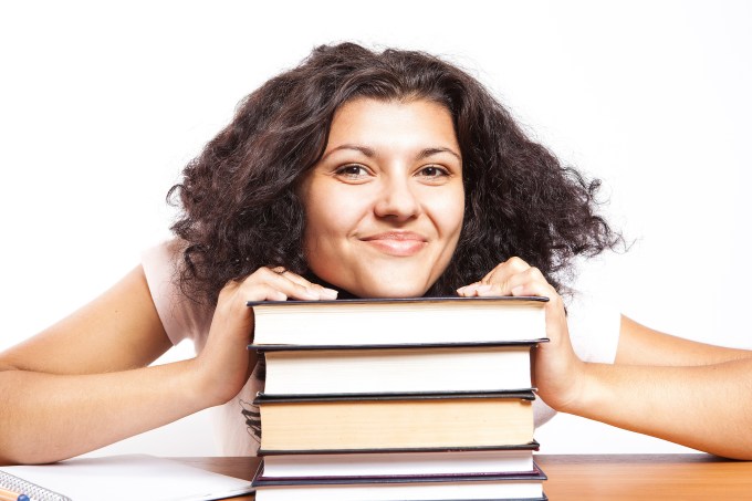 Estudante mulher sorri em cima de pilha de livros