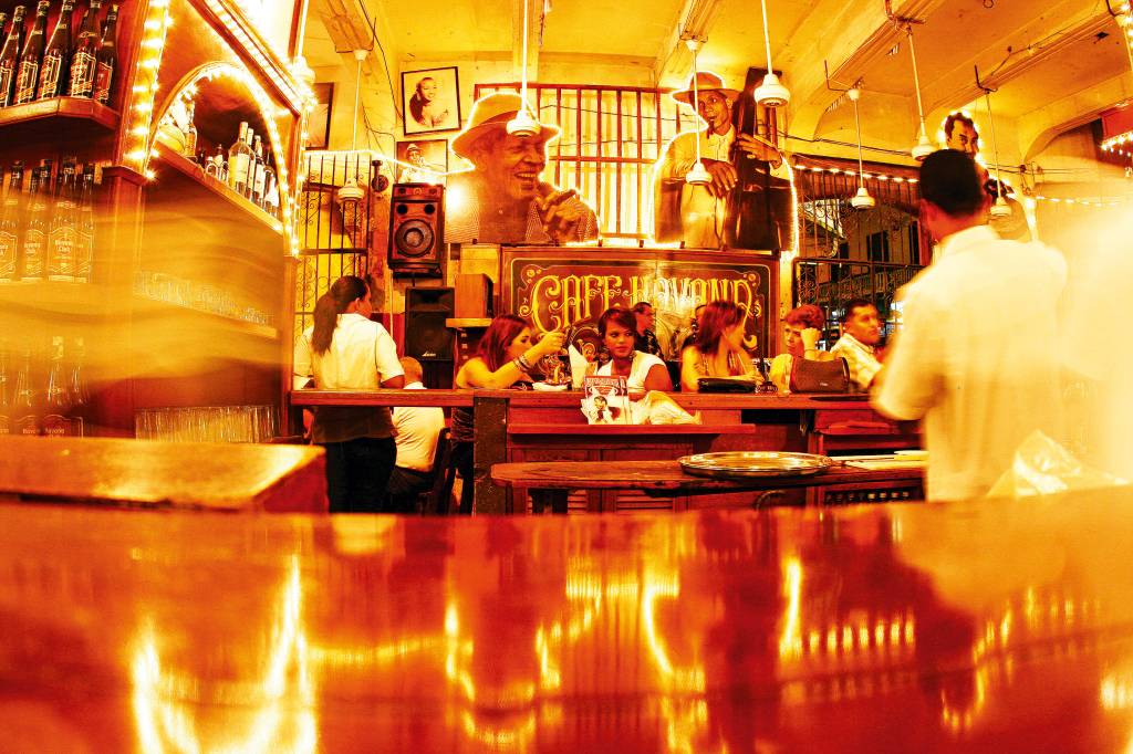 Interior de um café movimentado, com fotomontagens de personagens importantes para a salsa nas paredes