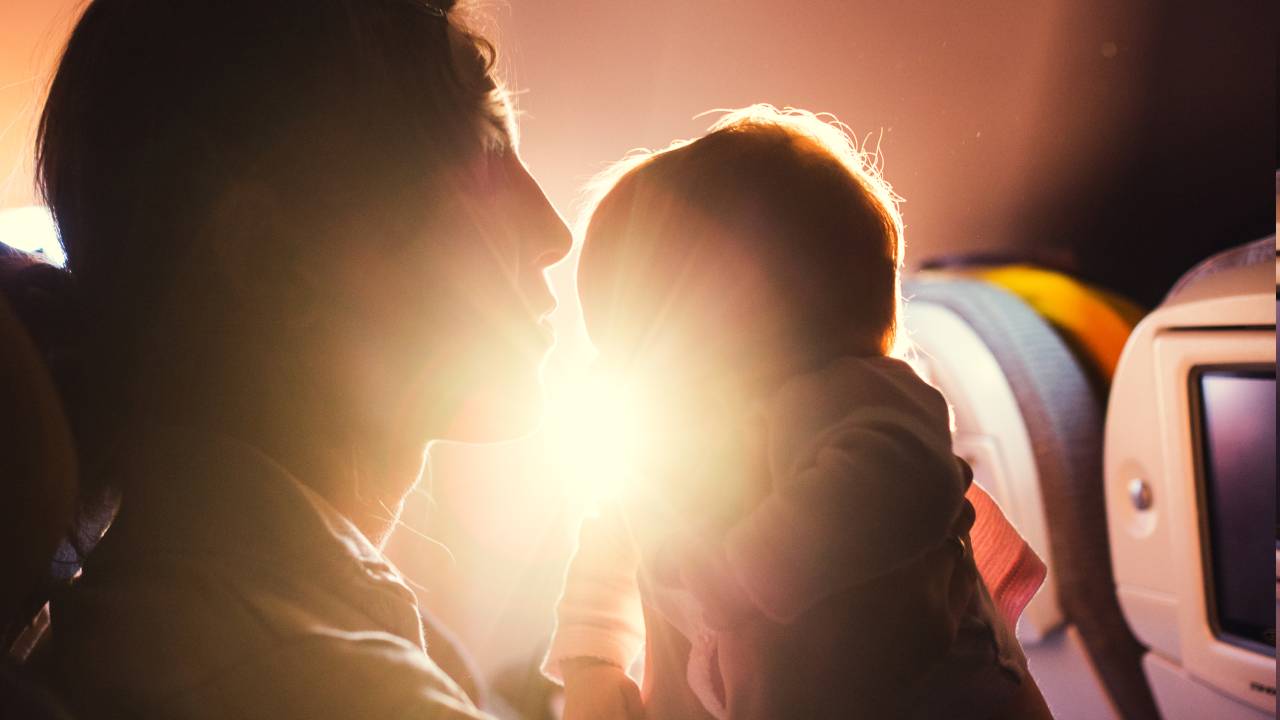 Mãe e bebê sentados em poltrona de avião durante voo comercial com sol ao fundo