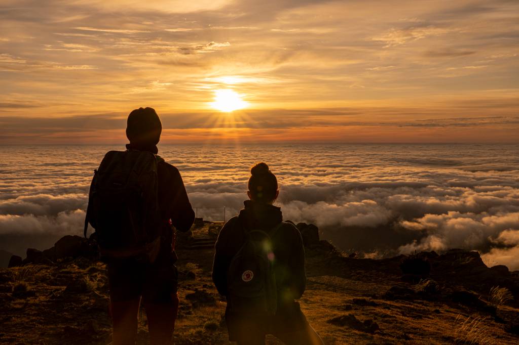 Duas pessoas observam o sol nascer acima das nuvens no Pico do Areeiro, Ilha da Madeira