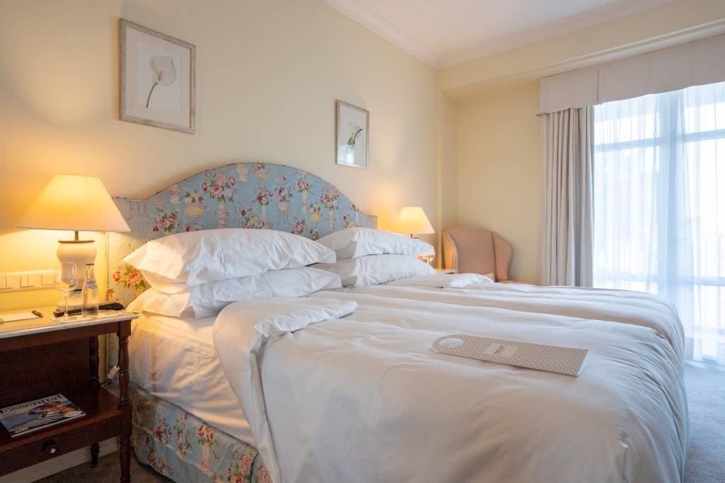 Quarto do hotel Reid's Palace, na Ilha da Madeira, com detalhe da cama com travesseiros, edredons e a cabeceira azul florida