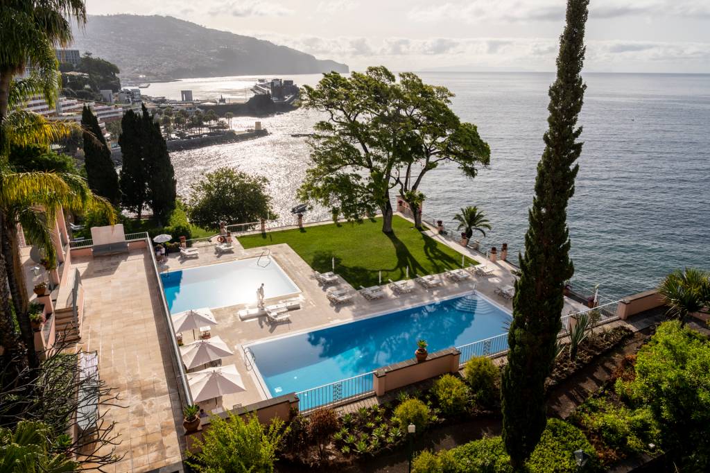 Duas piscinas, uma árvore e o mar no hotel Reid's Palace, na Ilha da Madeira