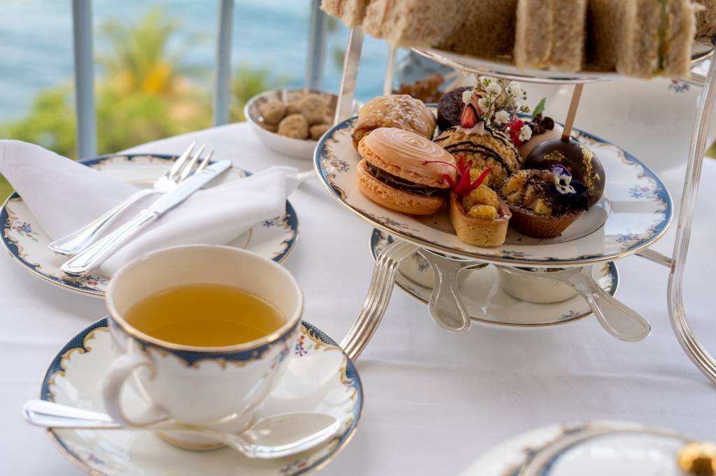 Xícara de chá e prato de doces em cima de uma mesa com vista do mar no hotel Reid's Palace, na Ilha da Madeira