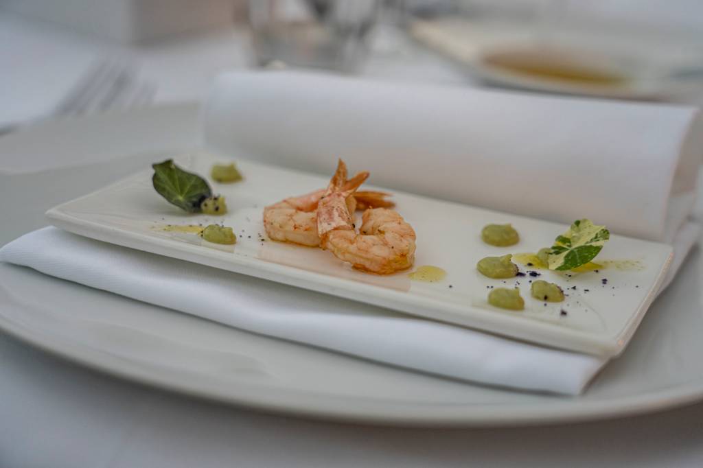 Prato branco com dois camarões e um molho verde na mesa do restaurante