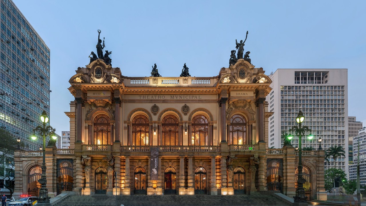 A imagem é uma foto da frente do Theatro Municipal de São Paulo, um prédio cuja arquitetura tem elementos barrocos, renascentistas de da Art Neuveau.