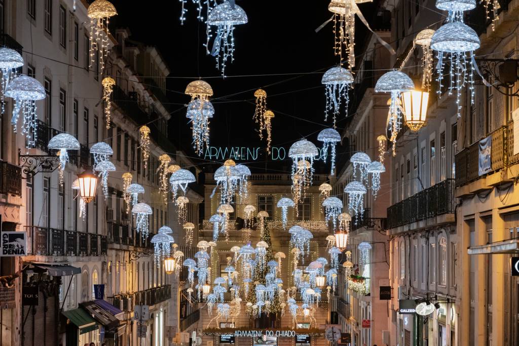33 Rua estreita, à noite, com dezenas de medusas de luz em azul e branco como enfeites de Natal
