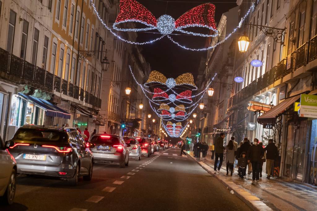 37 Rua com alguns carros passando, à noite, iluminada com grandes laços de luzes vermelhas e azuis para o Natal