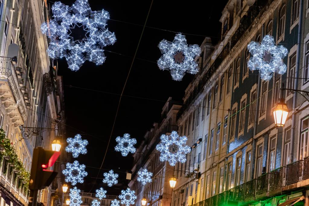 Rua de prédios coloridos, no escuro da noite, com iluminação em forma de grandes flocos de neve