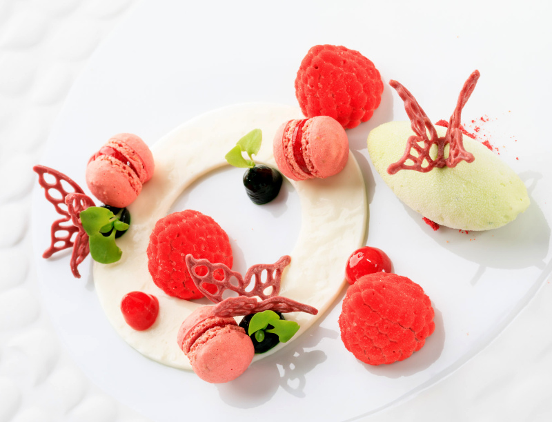 Sobremesa do restaurante Al Sud, no Algarve, servida em louça branca, onde se vê framboesas, mini macarons cor de rosa, detalhes verdes e sorvete