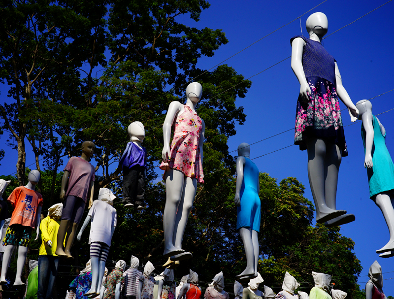 A imagem é uma foto tirada de baixo para cima, numa ângulo em que vemos um céu límpido e manequins com diferentes roupas preenchendo sua limpidez.