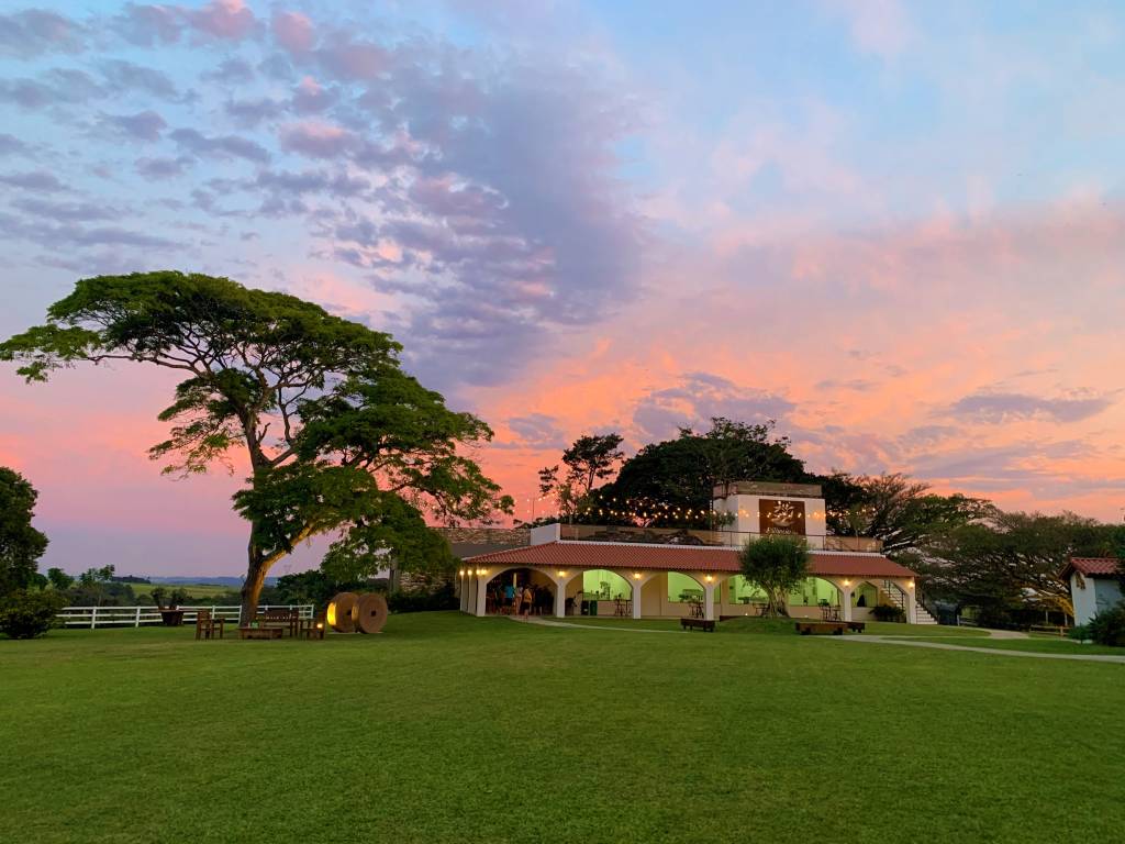 Lagar da Estância das Oliveiras Na imagem vemos uma construção, que parece uma casa grande, em meio à um campo verde.