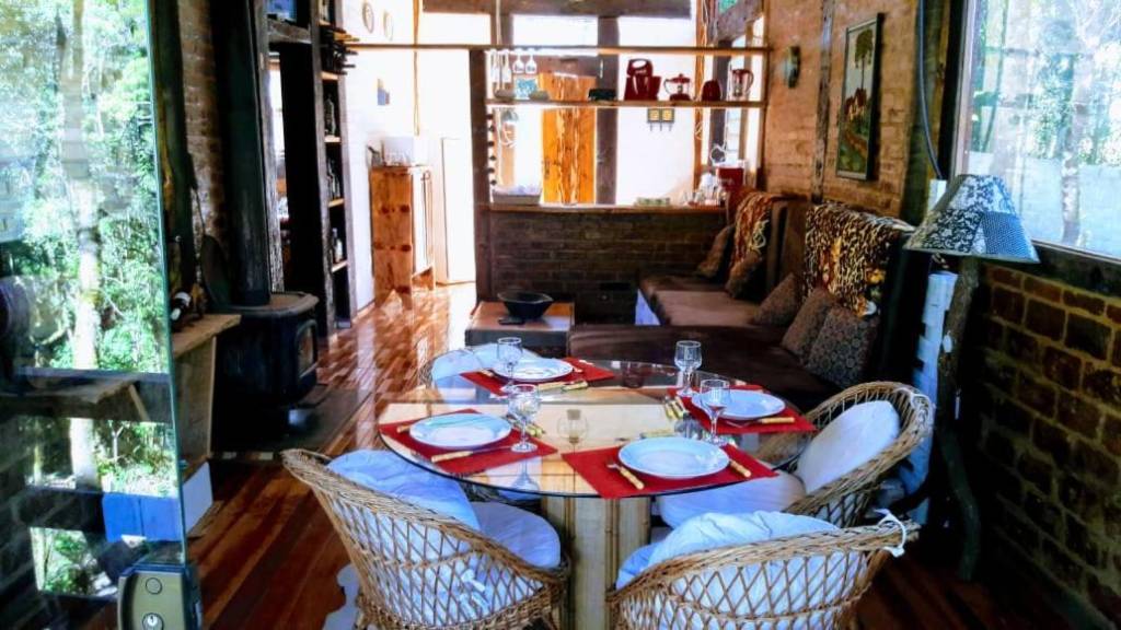Rustic House, Campos do Jordão, São Paulo A imagem mostra uma sala com paredes de tijolos, mobiliada com móveis rústicos