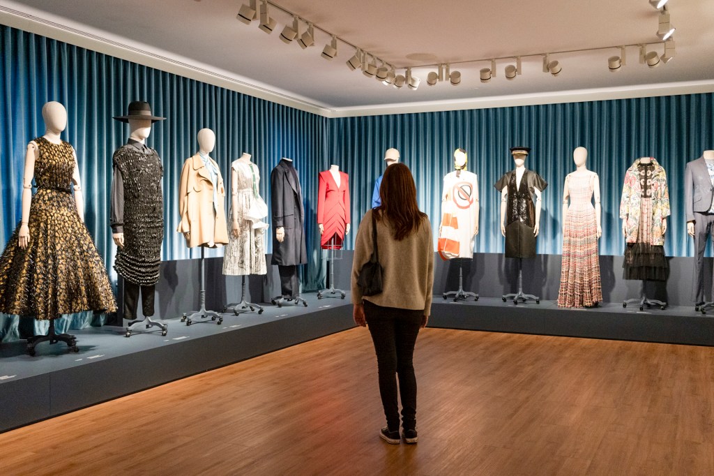 Pessoa de costas parada em frente a uma exposição de moda com manequins vestindo roupas coloridas