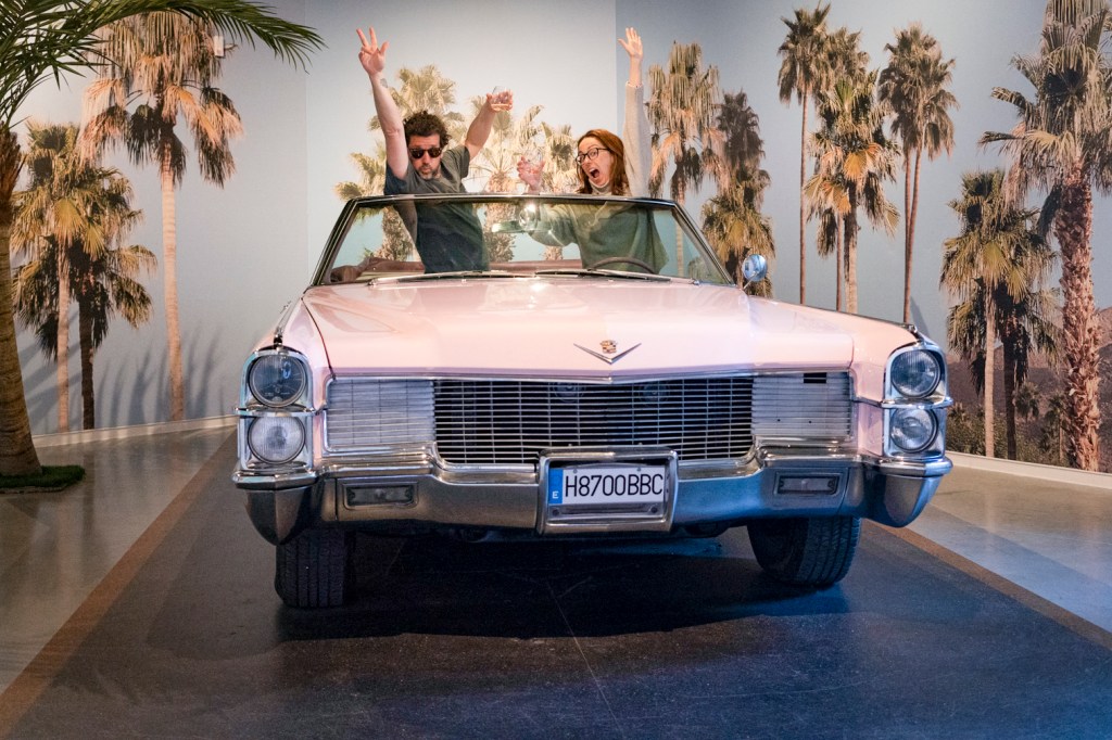 Casal posa em um cadillac conversível cor de rosa