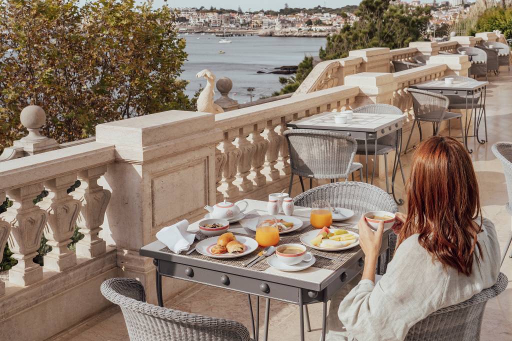 38 Mesa de café da manhã com vista do mar e uma mulher sentada de costas