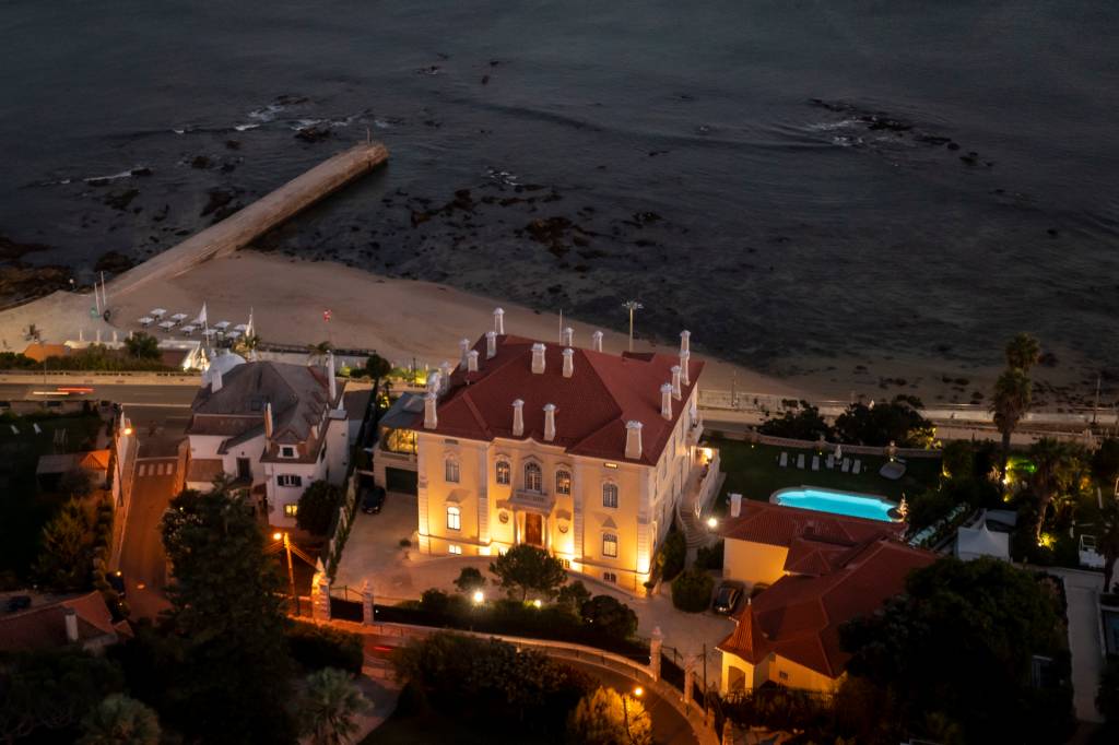 DJI_0951 Vista aérea de um palacete amarelo com piscina à beira-mar, ao anoitecer
