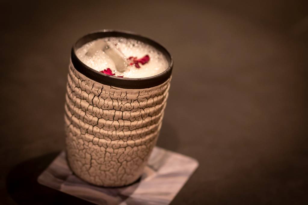 Drink do bar do restaurante japonês kKabuki, servido em um copo de cerâmica e coroado com uma espuma e pétalas de flor