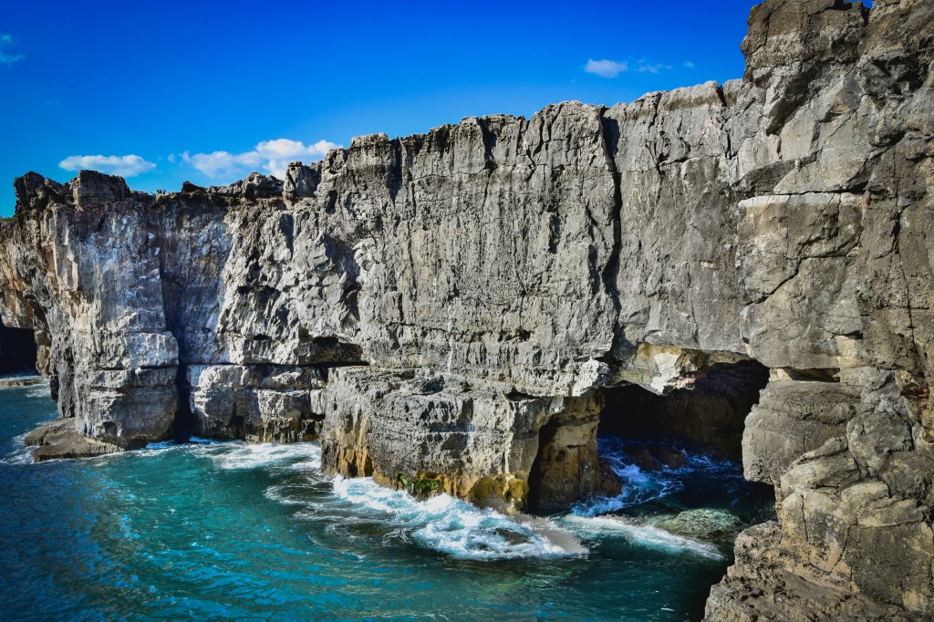 Falésias que formam um paredão íngreme junto a um mar de águas verde-esmeralda