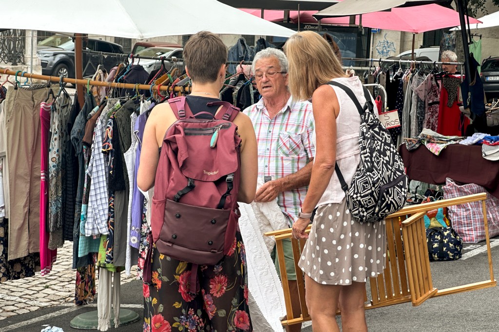 Casal de estrangeiros conversa com o dono de uma barraca de roupas na Feira da Ladra