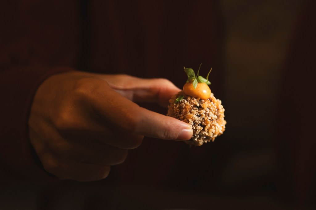 Fotografia colorida mostra uma mão segurando um croquete